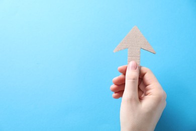 Photo of Woman with paper arrow on light blue background, top view. Space for text