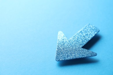 Photo of One glitter arrow on light blue background, closeup. Space for text