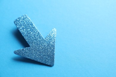 Photo of One glitter arrow on light blue background, closeup. Space for text