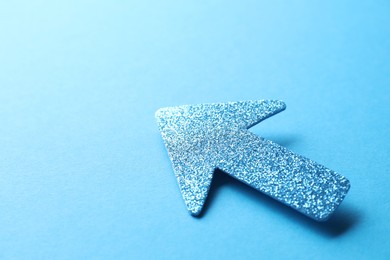 Photo of One glitter arrow on light blue background, closeup. Space for text