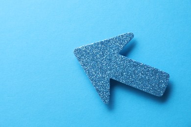 Photo of One glitter arrow on light blue background, top view. Space for text