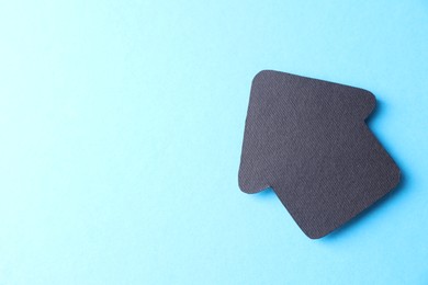 Photo of One black paper arrow on light blue background, top view. Space for text