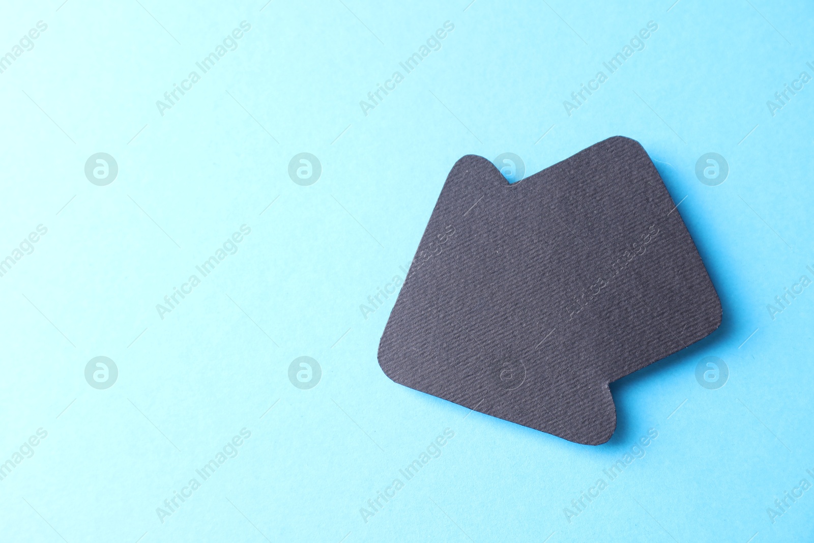 Photo of One black paper arrow on light blue background, top view. Space for text