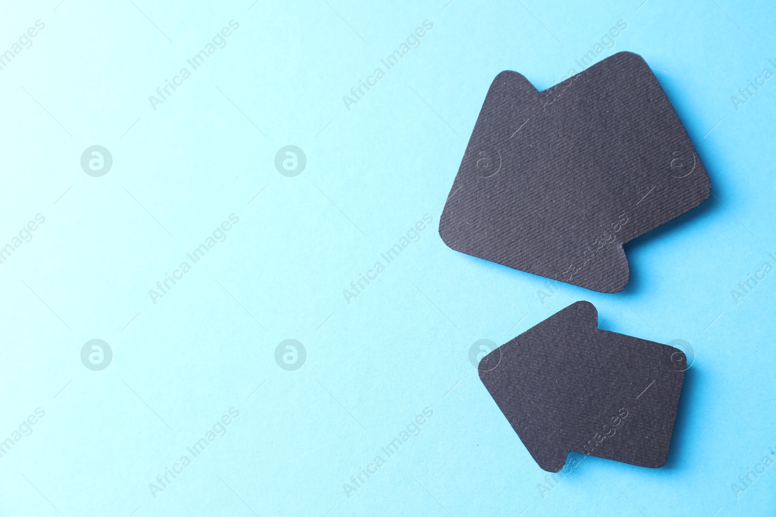 Photo of Two black paper arrows on light blue background, top view. Space for text