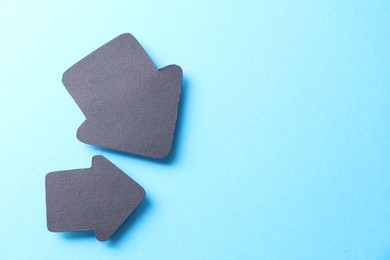 Photo of Two black paper arrows on light blue background, top view. Space for text