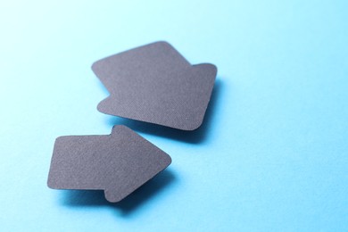 Photo of Two black paper arrows on light blue background, closeup