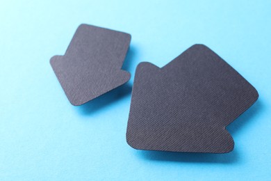 Photo of Two black paper arrows on light blue background, closeup