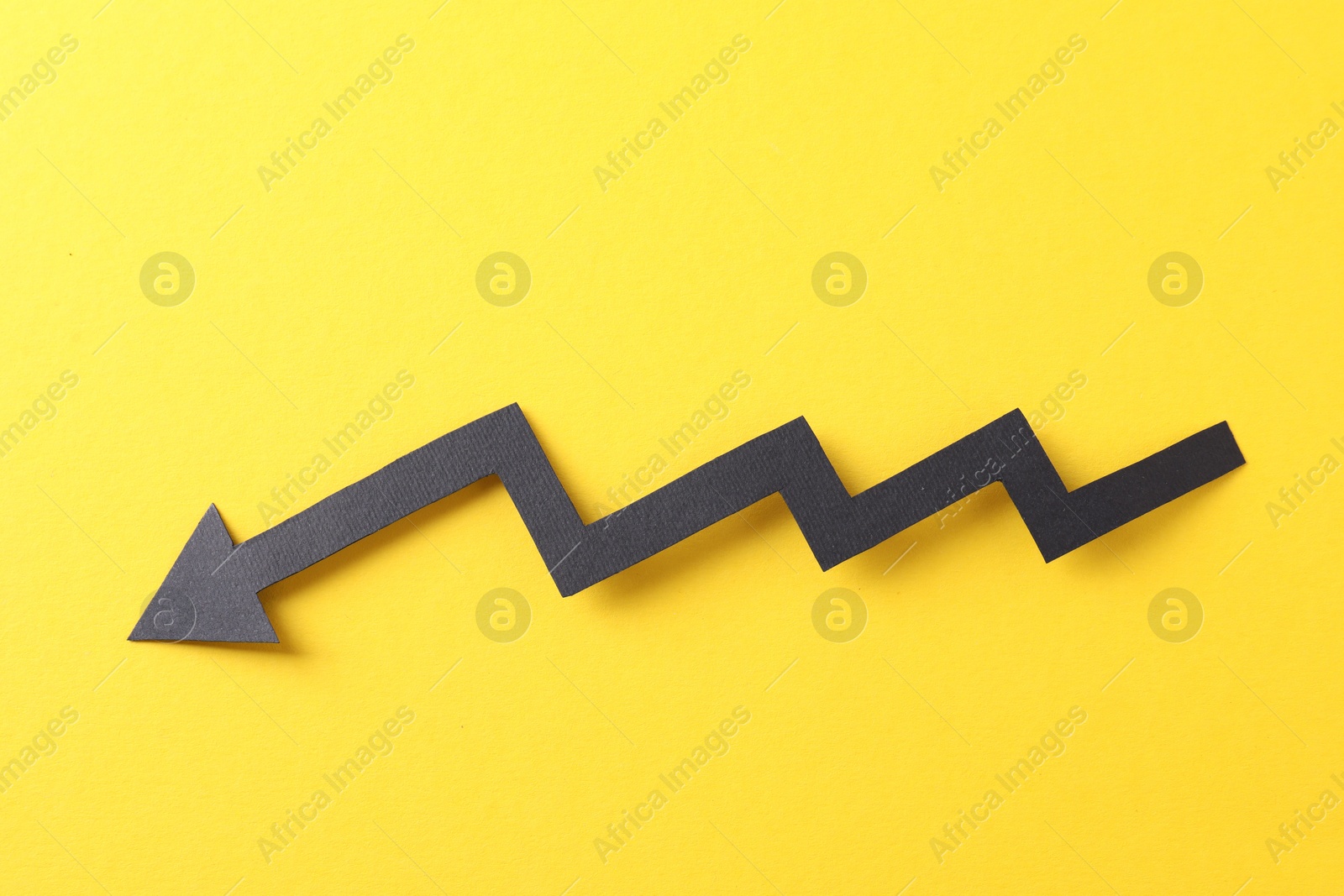 Photo of One black paper arrow on yellow background, top view