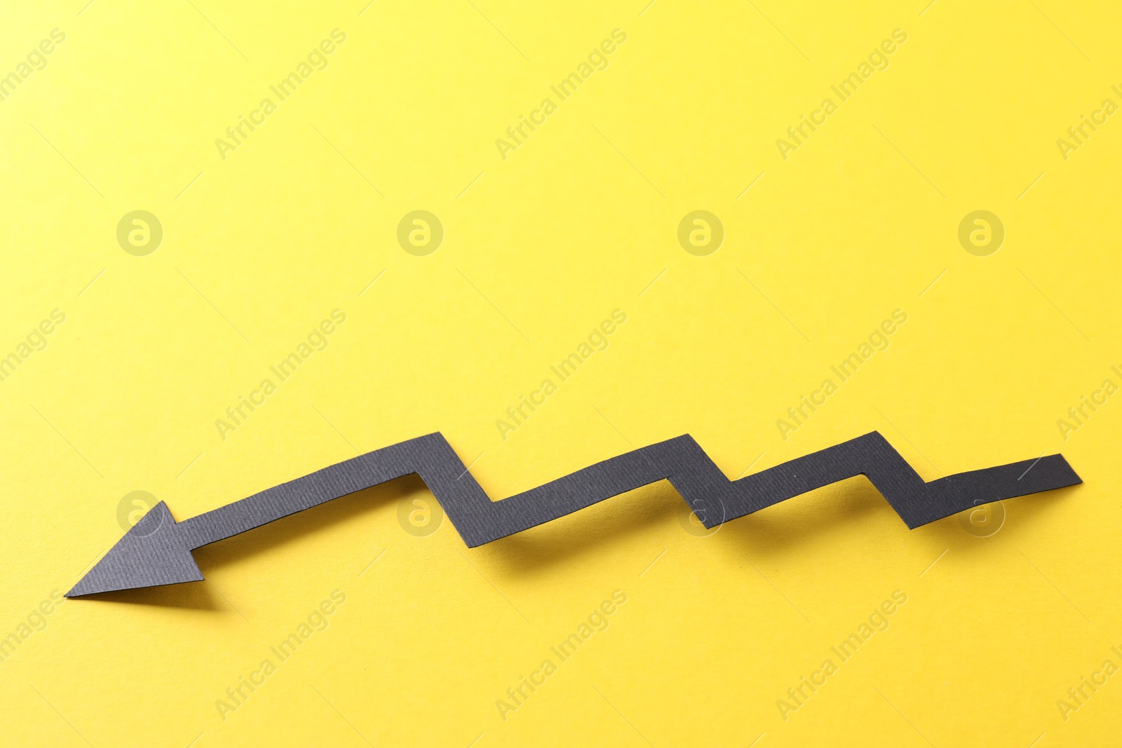 Photo of One black paper arrow on yellow background. Space for text