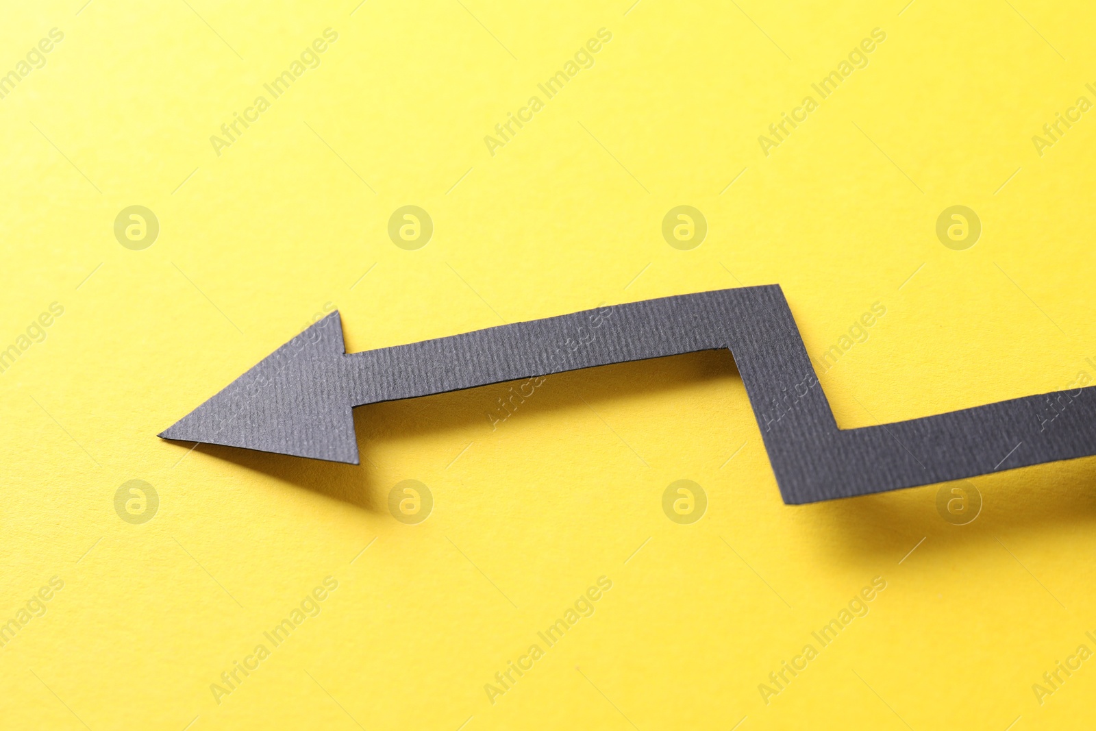 Photo of One black paper arrow on yellow background, closeup