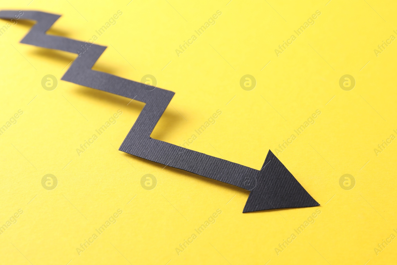 Photo of One black paper arrow on yellow background, closeup