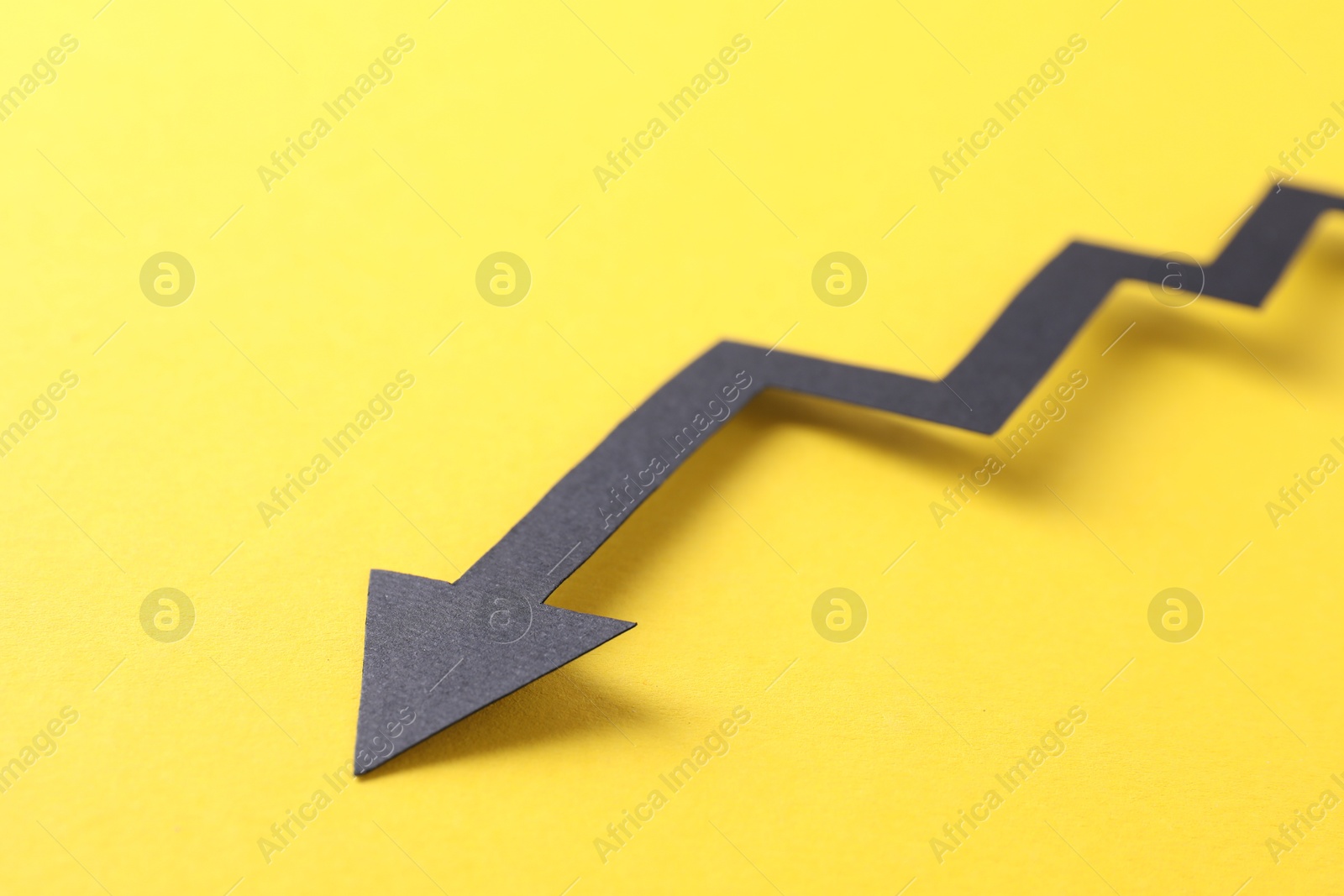 Photo of One black paper arrow on yellow background, closeup