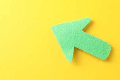 Photo of One green arrow on yellow background, top view. Space for text