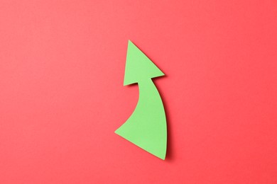 Photo of One green paper arrow on red background, top view