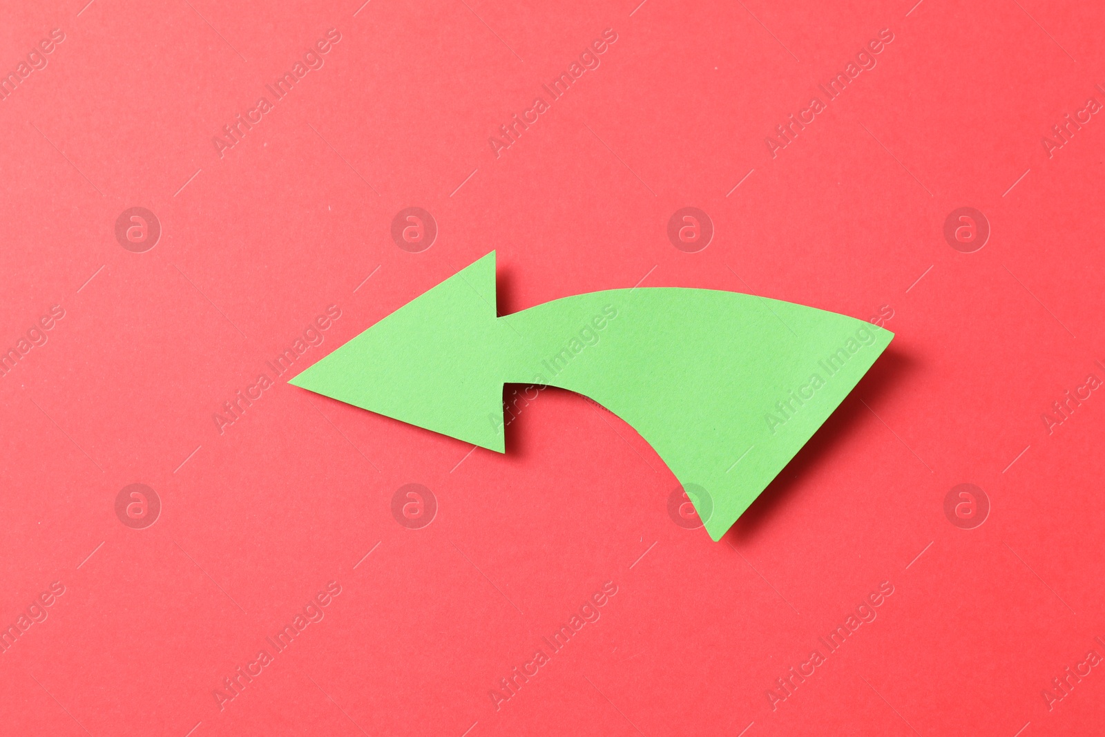 Photo of One green paper arrow on red background, top view