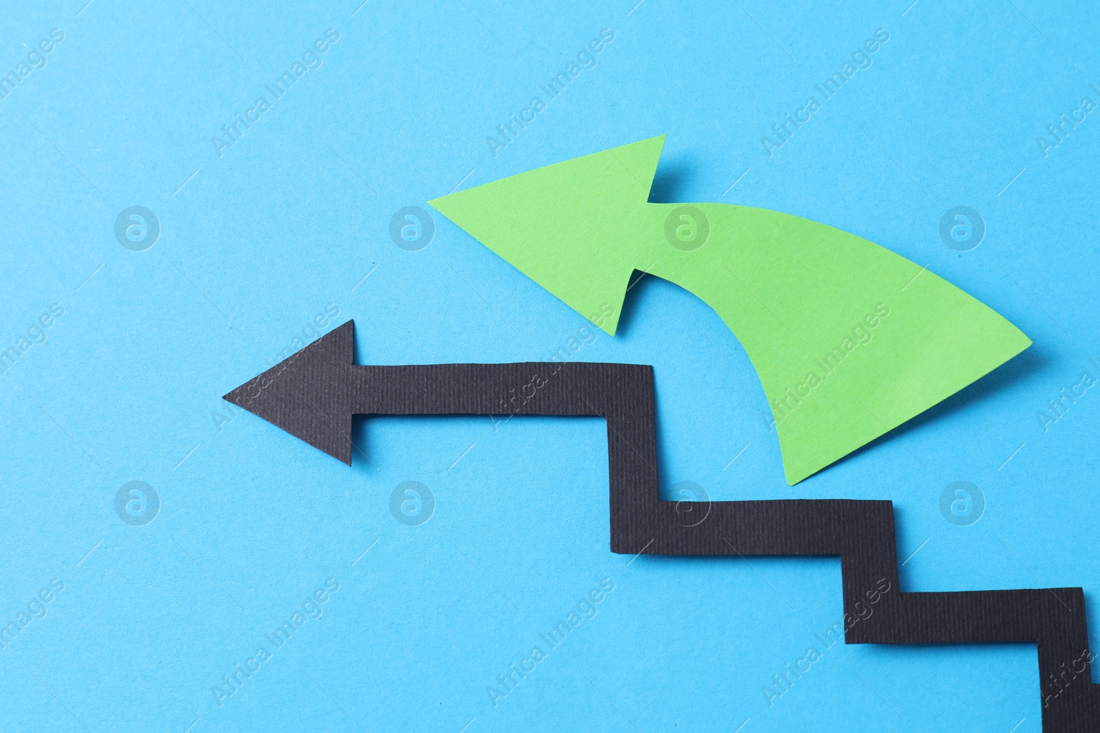 Photo of Two color paper arrows on light blue background, closeup