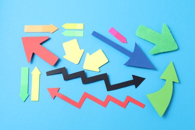 Photo of Different paper arrows on light blue background, flat lay