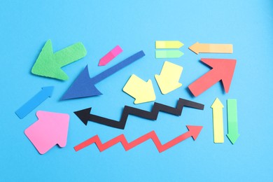 Photo of Different paper arrows on light blue background, flat lay