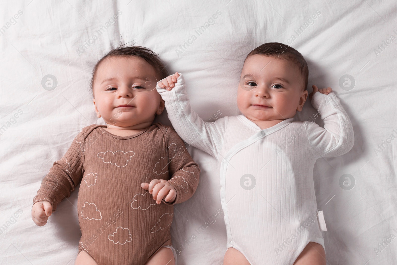 Photo of Cute twin babies resting on bed indoors, top view