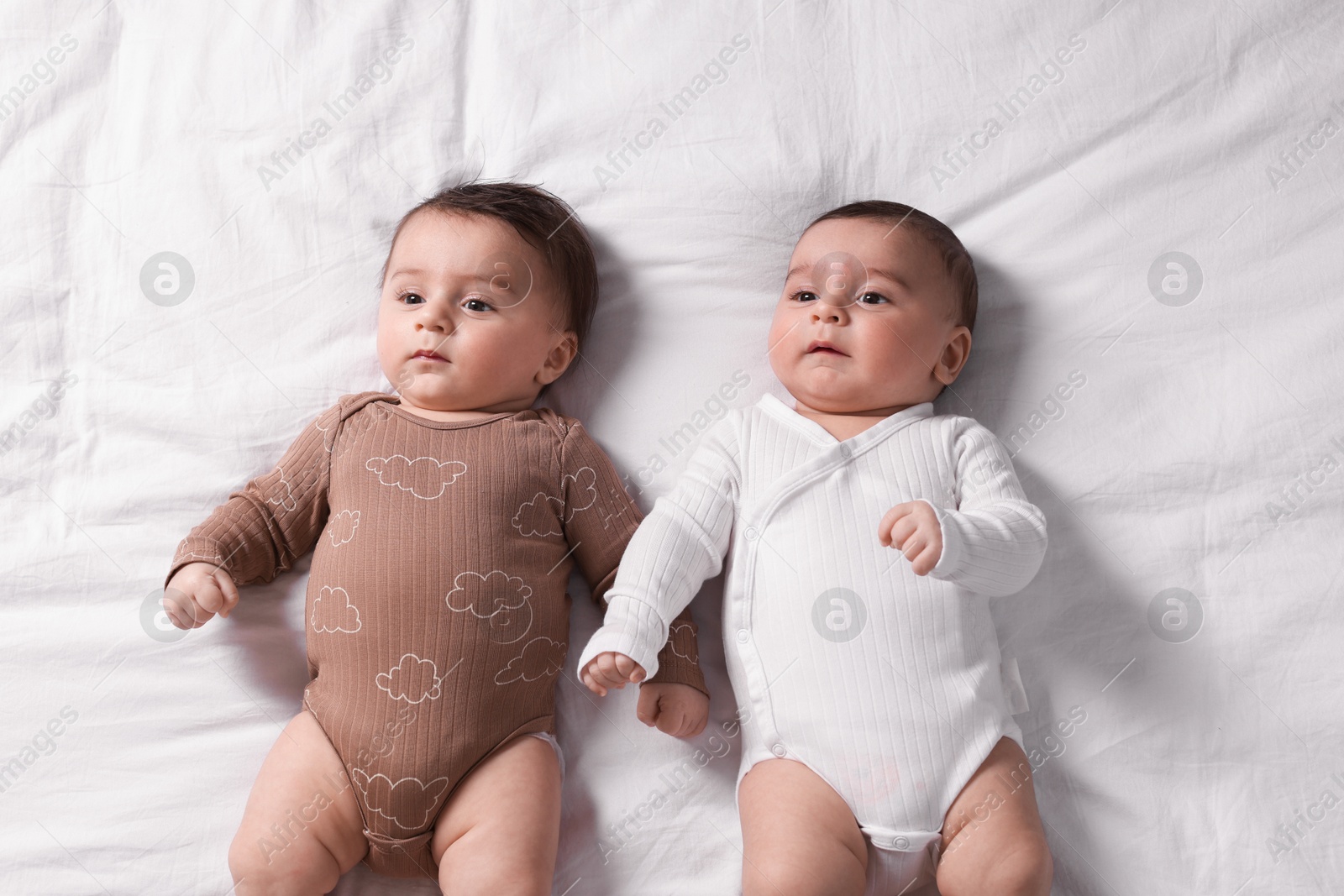 Photo of Cute twin babies resting on bed indoors, top view