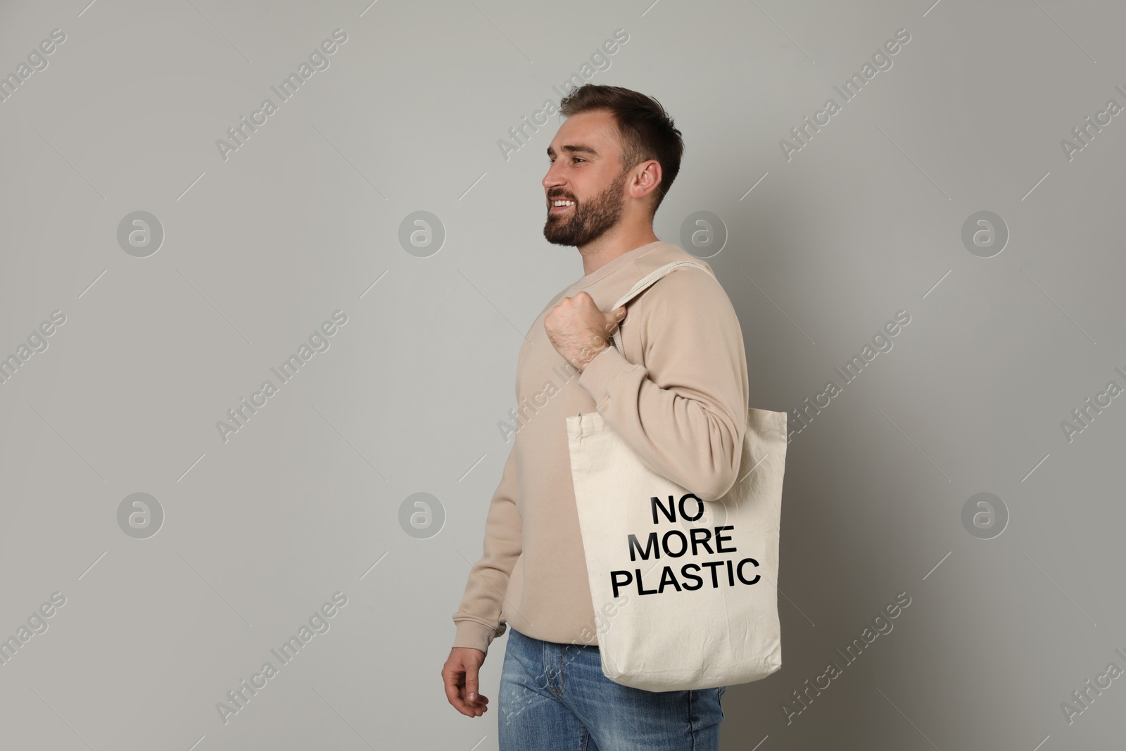 Image of Happy young man holding eco bag with No More Plastic text on light background