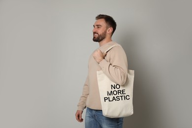 Image of Happy young man holding eco bag with No More Plastic text on light background