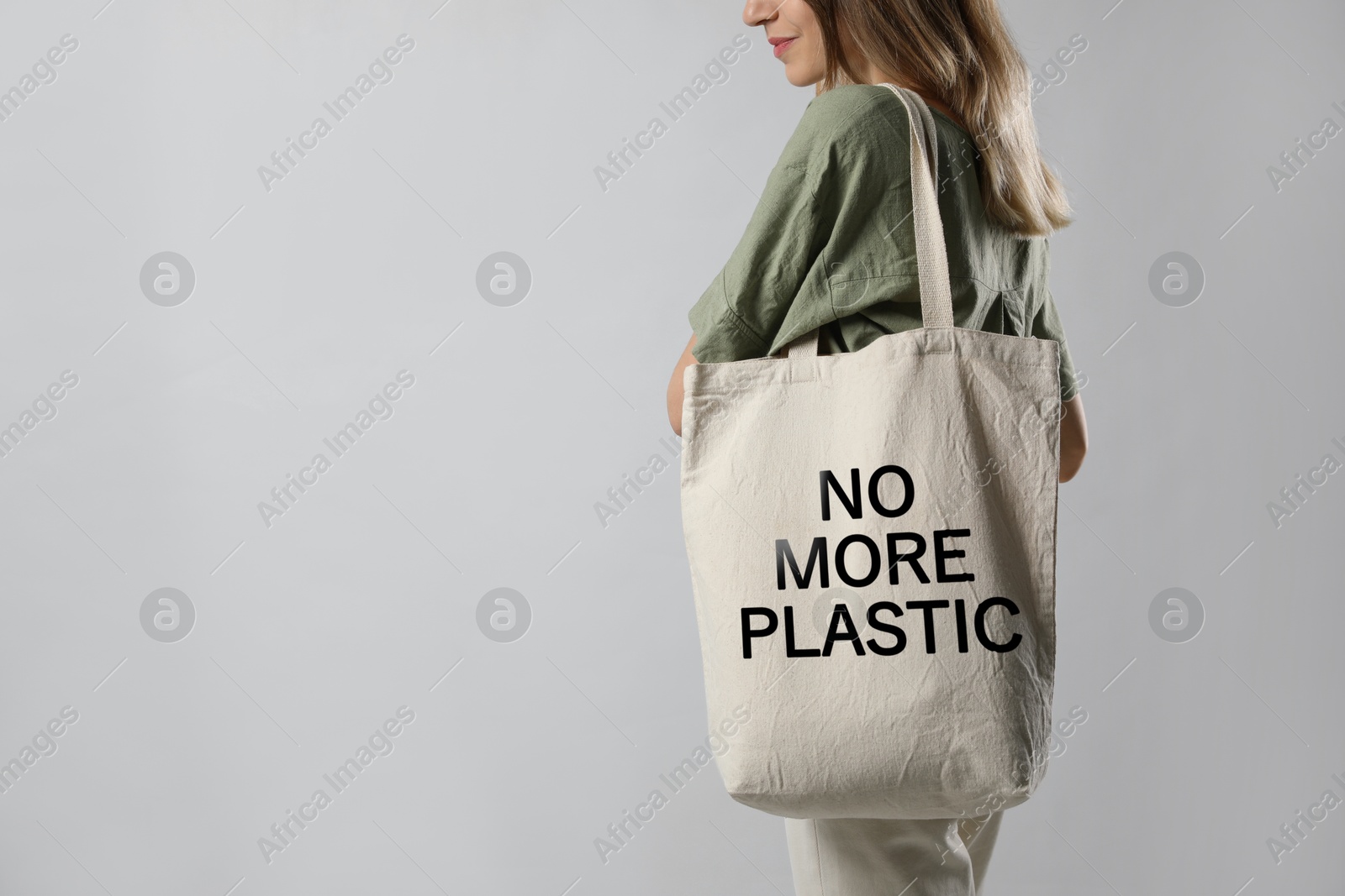 Image of Young woman holding eco bag with No More Plastic text on light grey background, closeup