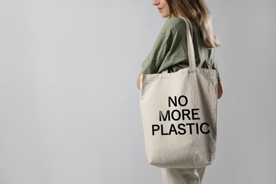 Young woman holding eco bag with No More Plastic text on light grey background, closeup