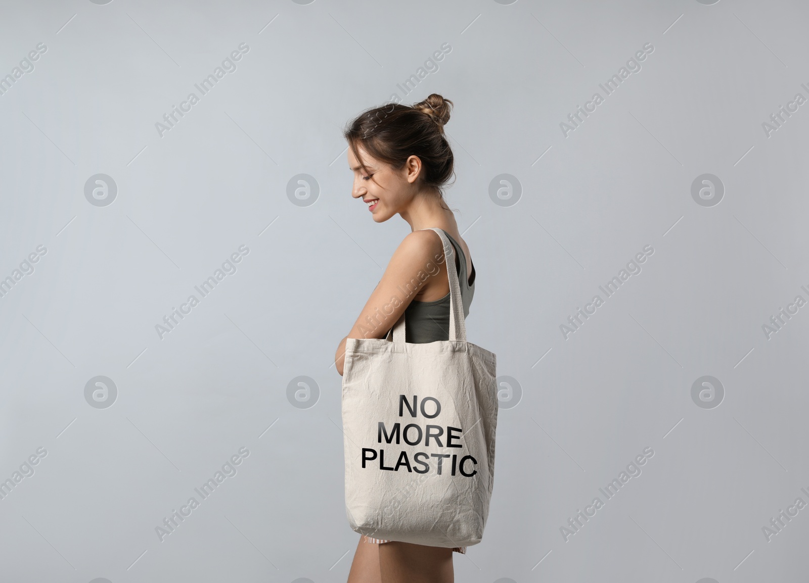 Image of Happy young woman holding eco bag with No More Plastic text on light grey background