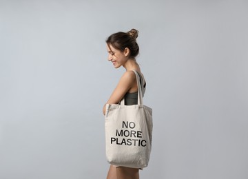 Image of Happy young woman holding eco bag with No More Plastic text on light grey background