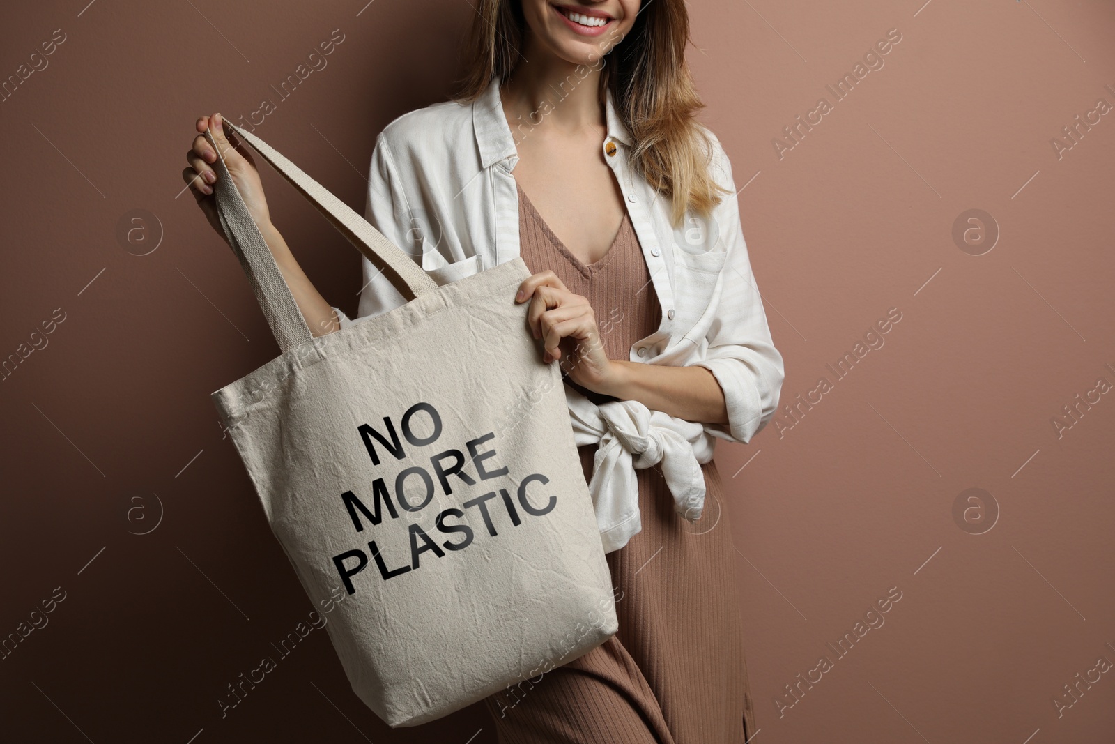 Image of Happy young woman holding eco bag with No More Plastic text on dark beige background, closeup