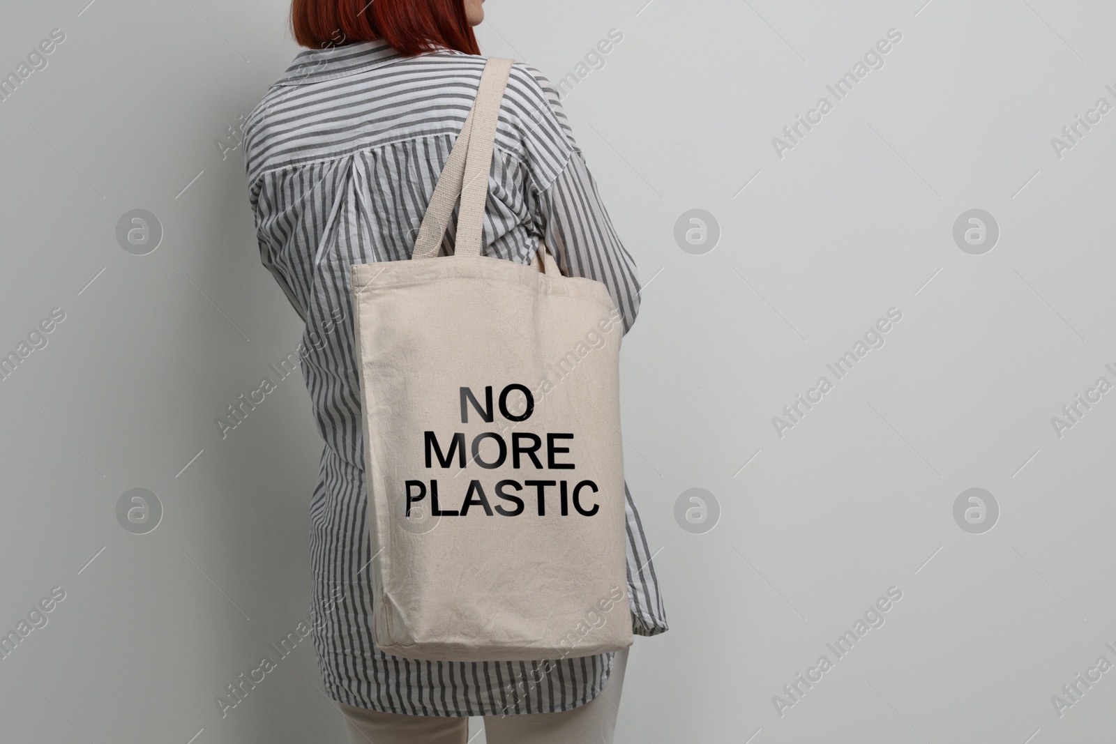 Image of Woman holding eco bag with No More Plastic text on light background, closeup