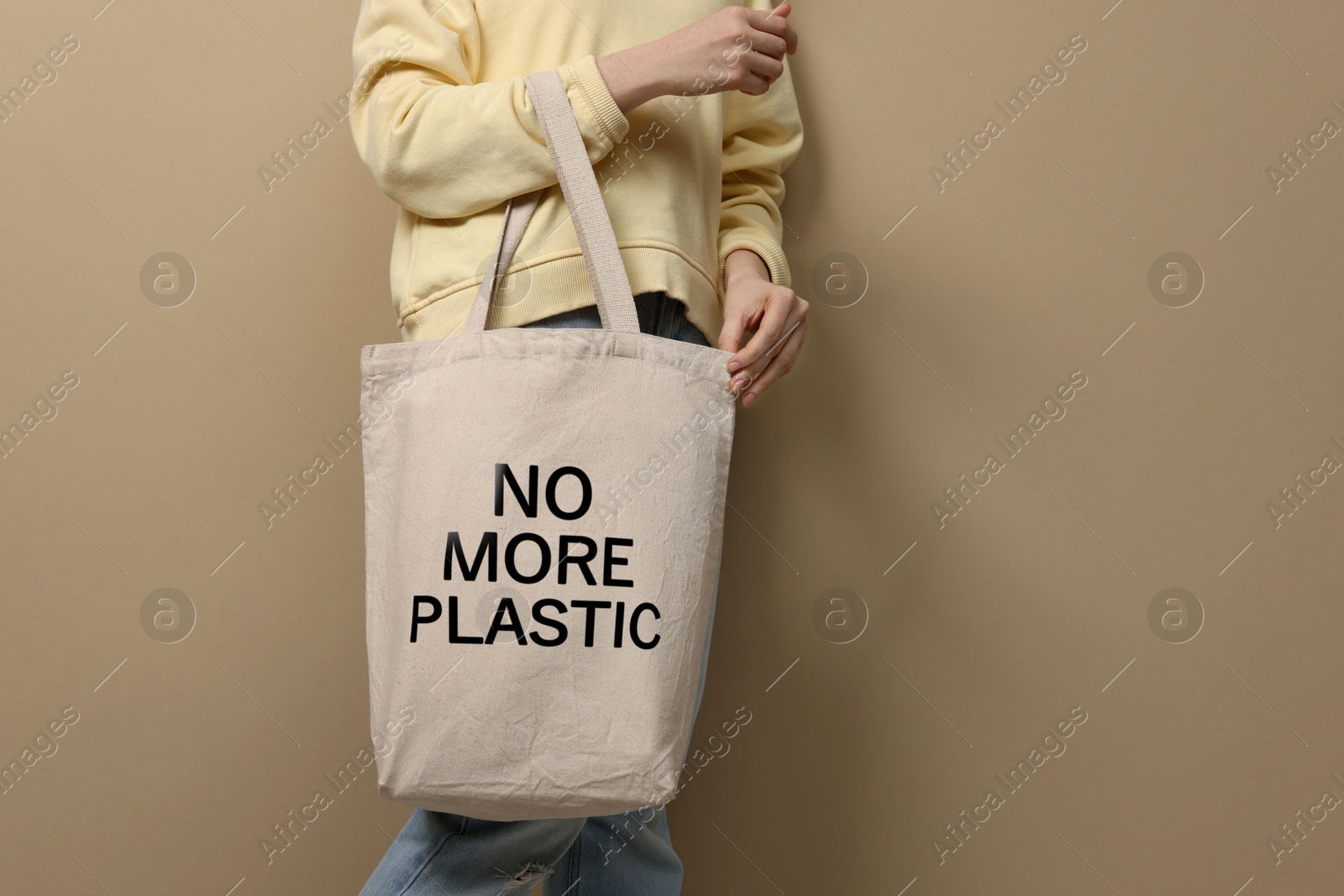 Image of Woman holding eco bag with No More Plastic text on dark beige background, closeup