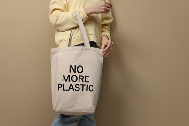 Image of Woman holding eco bag with No More Plastic text on dark beige background, closeup