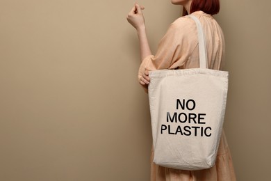 Image of Young woman holding eco bag with No More Plastic text on dark beige background, closeup