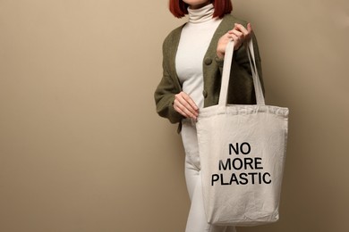 Image of Young woman holding eco bag with No More Plastic text on dark beige background, closeup