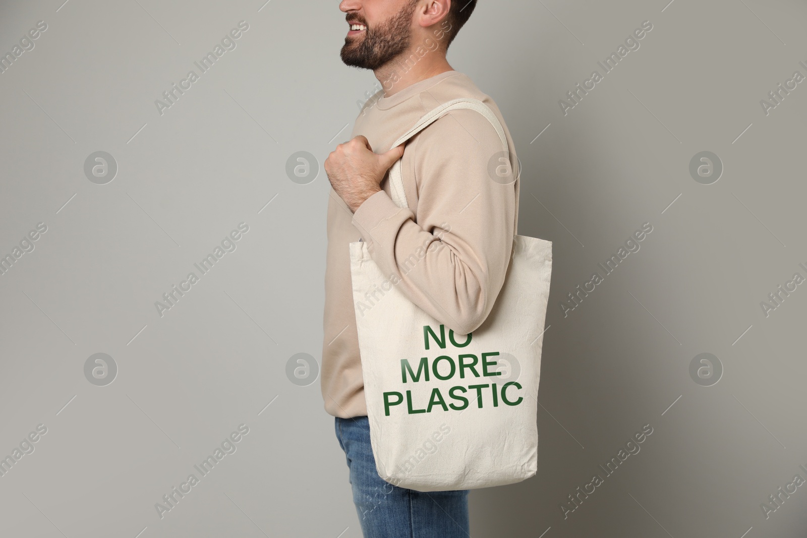 Image of Happy young man holding eco bag with No More Plastic text on light background, closeup