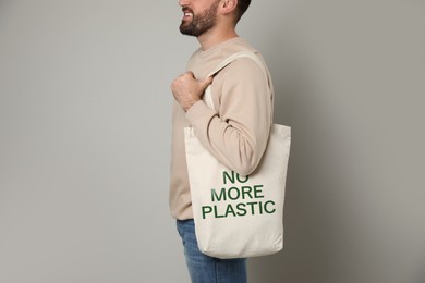 Happy young man holding eco bag with No More Plastic text on light background, closeup