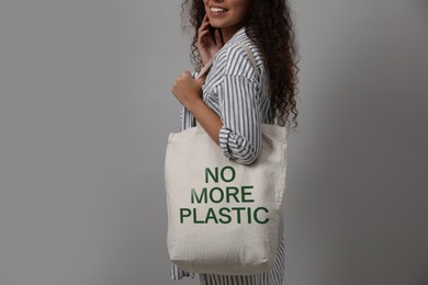 Image of Happy young woman holding eco bag with No More Plastic text on light grey background, closeup