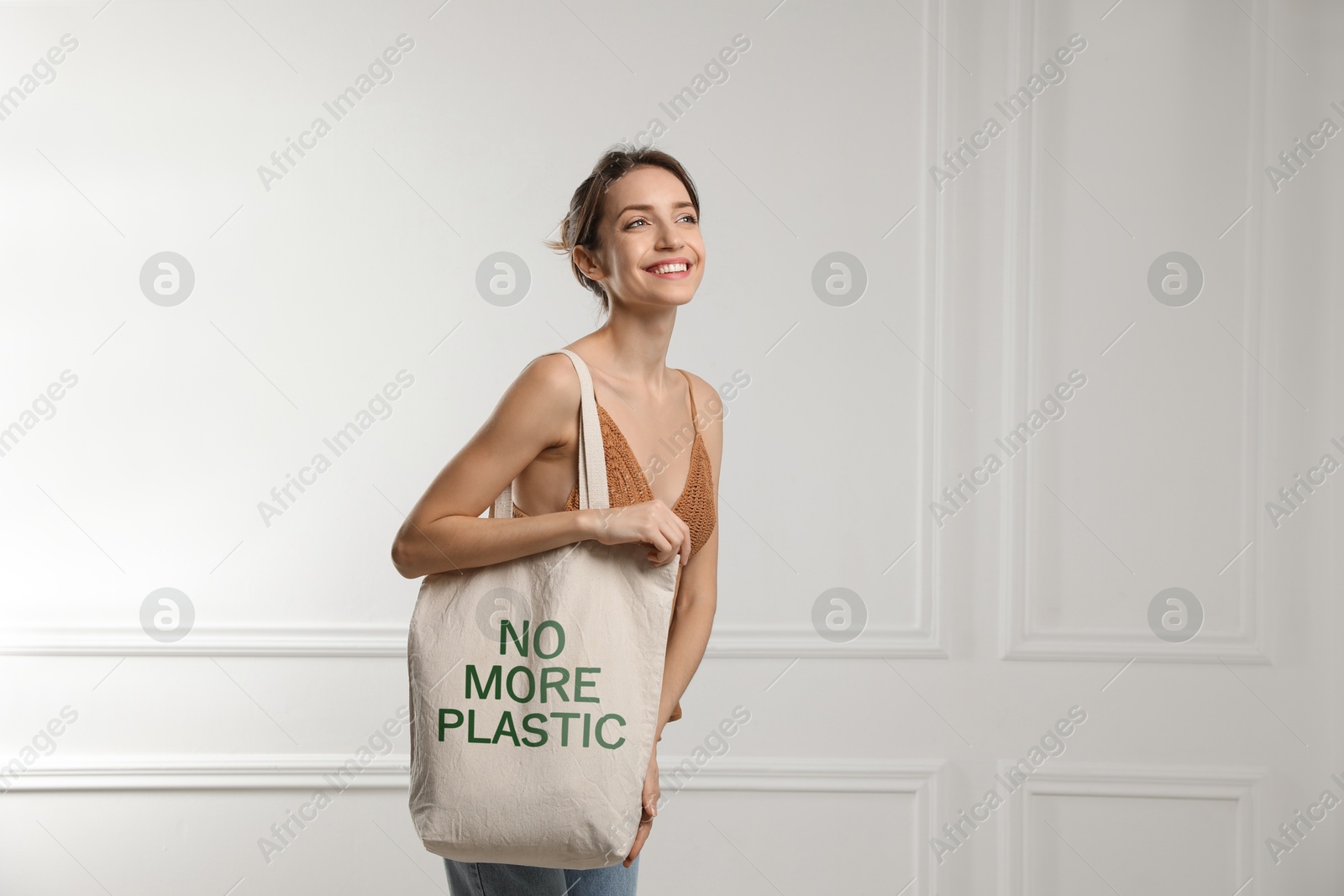 Image of Happy young woman holding eco bag with No More Plastic text indoors