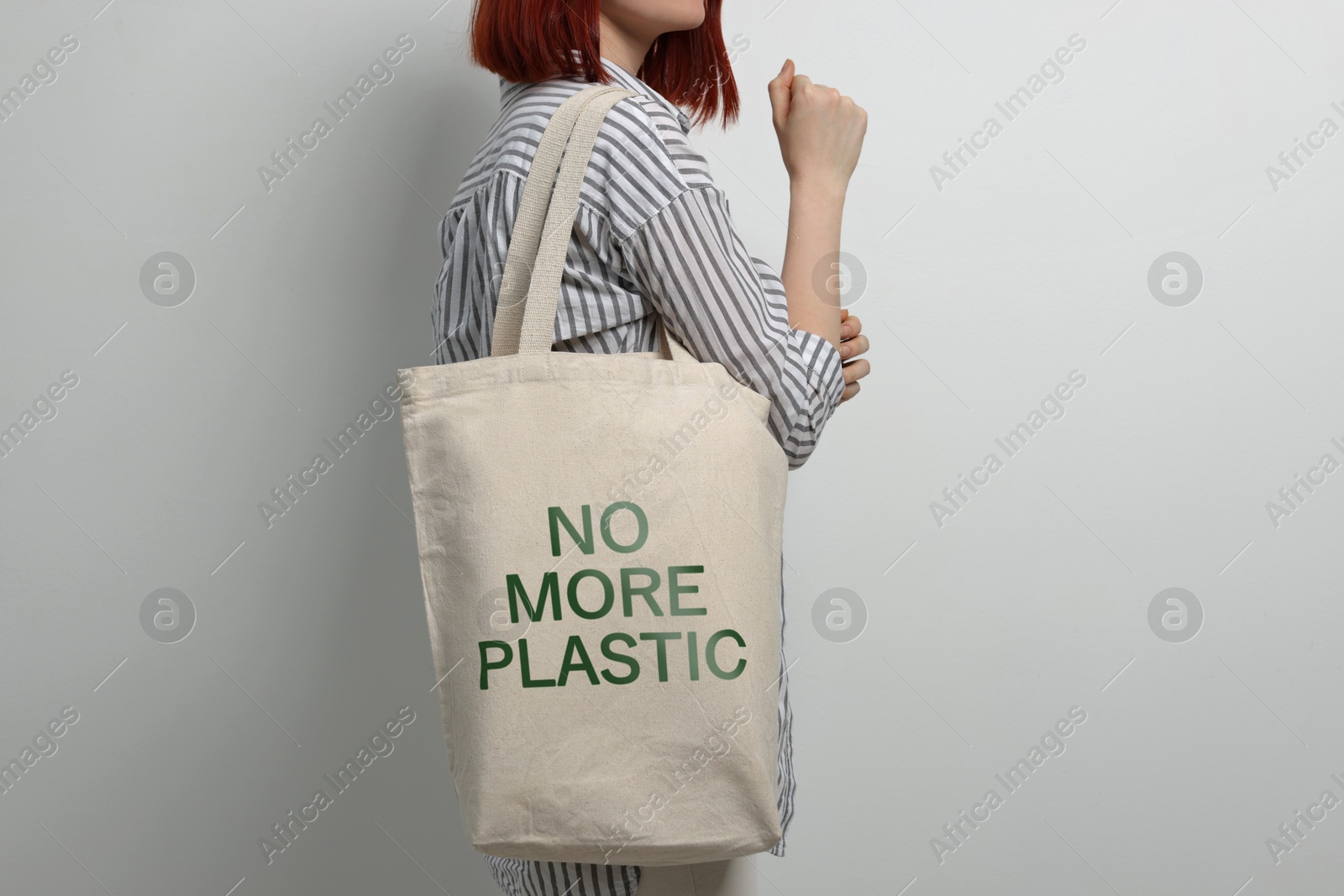 Image of Young woman holding eco bag with No More Plastic text on light background, closeup