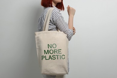 Image of Young woman holding eco bag with No More Plastic text on light background, closeup