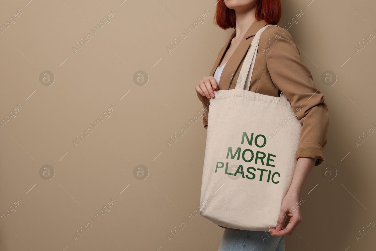 Image of Young woman holding eco bag with No More Plastic text on dark beige background, closeup