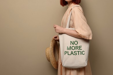 Image of Young woman holding eco bag with No More Plastic text on dark beige background, closeup