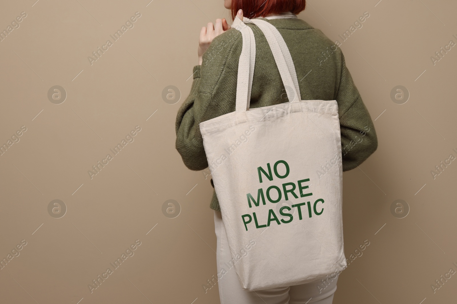 Image of Young woman holding eco bag with No More Plastic text on dark beige background, closeup