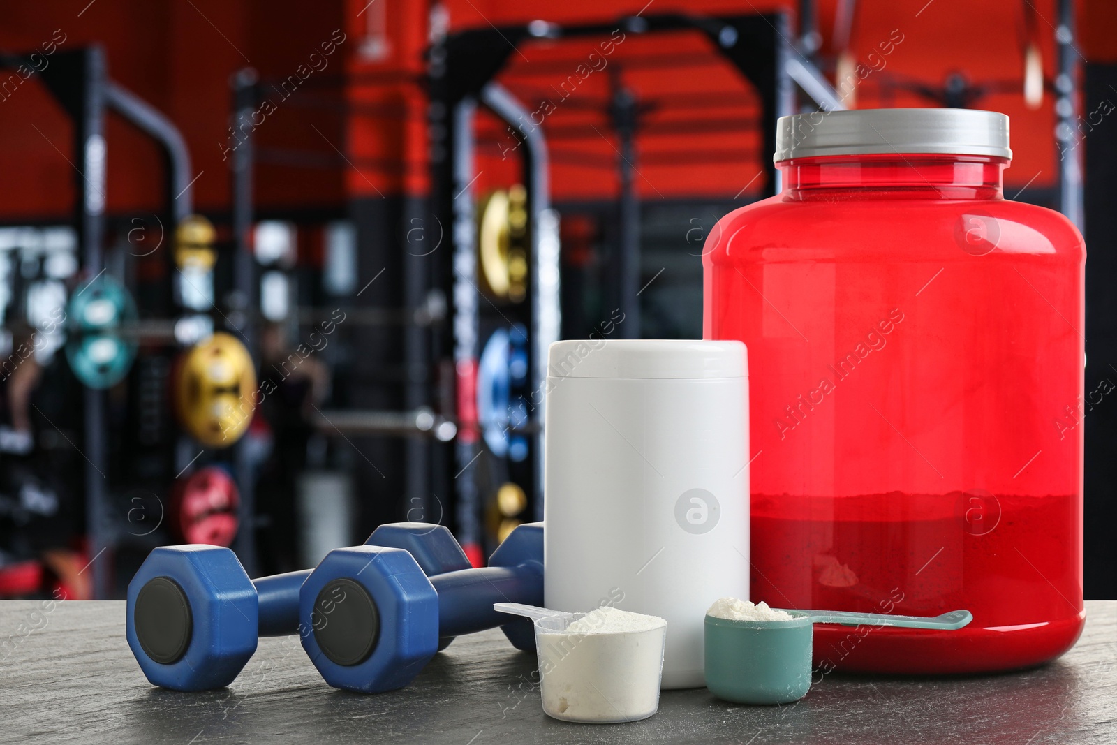 Image of Protein powder and dumbbells on grey table in gym, space for text