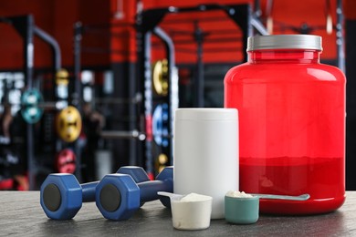 Image of Protein powder and dumbbells on grey table in gym, space for text