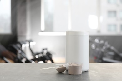 Protein powder on grey table in gym, space for text