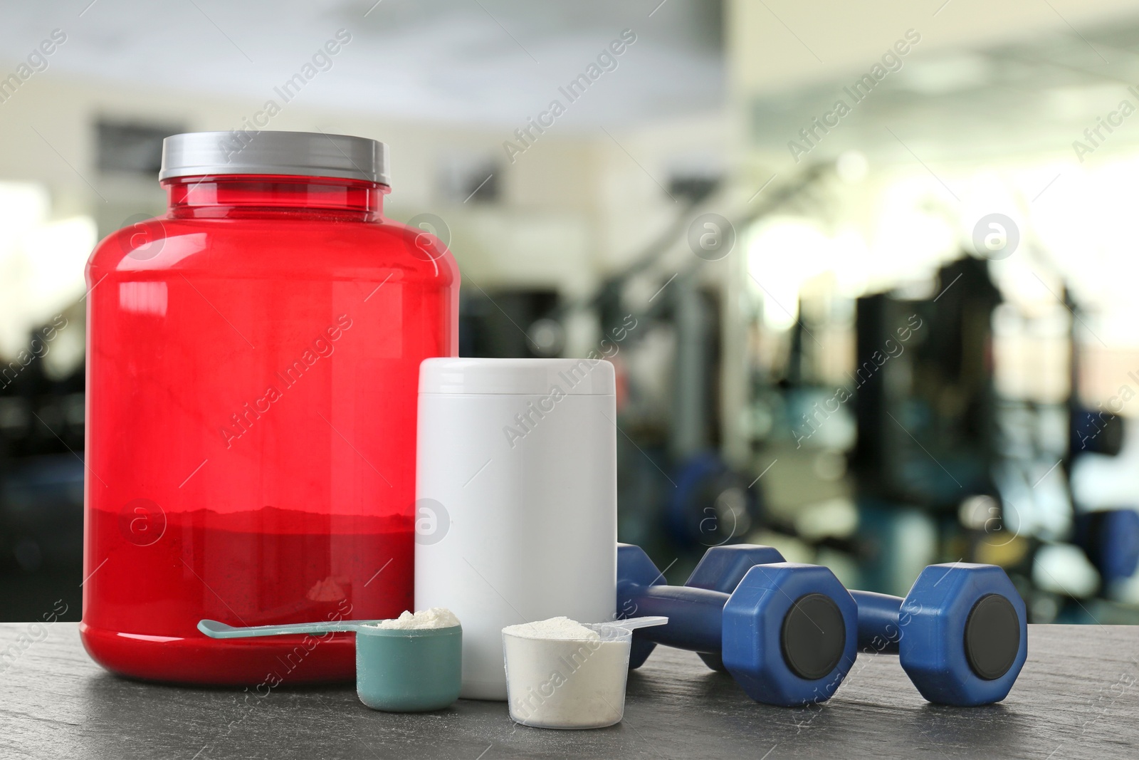 Image of Protein powder and dumbbells on grey table in gym, space for text