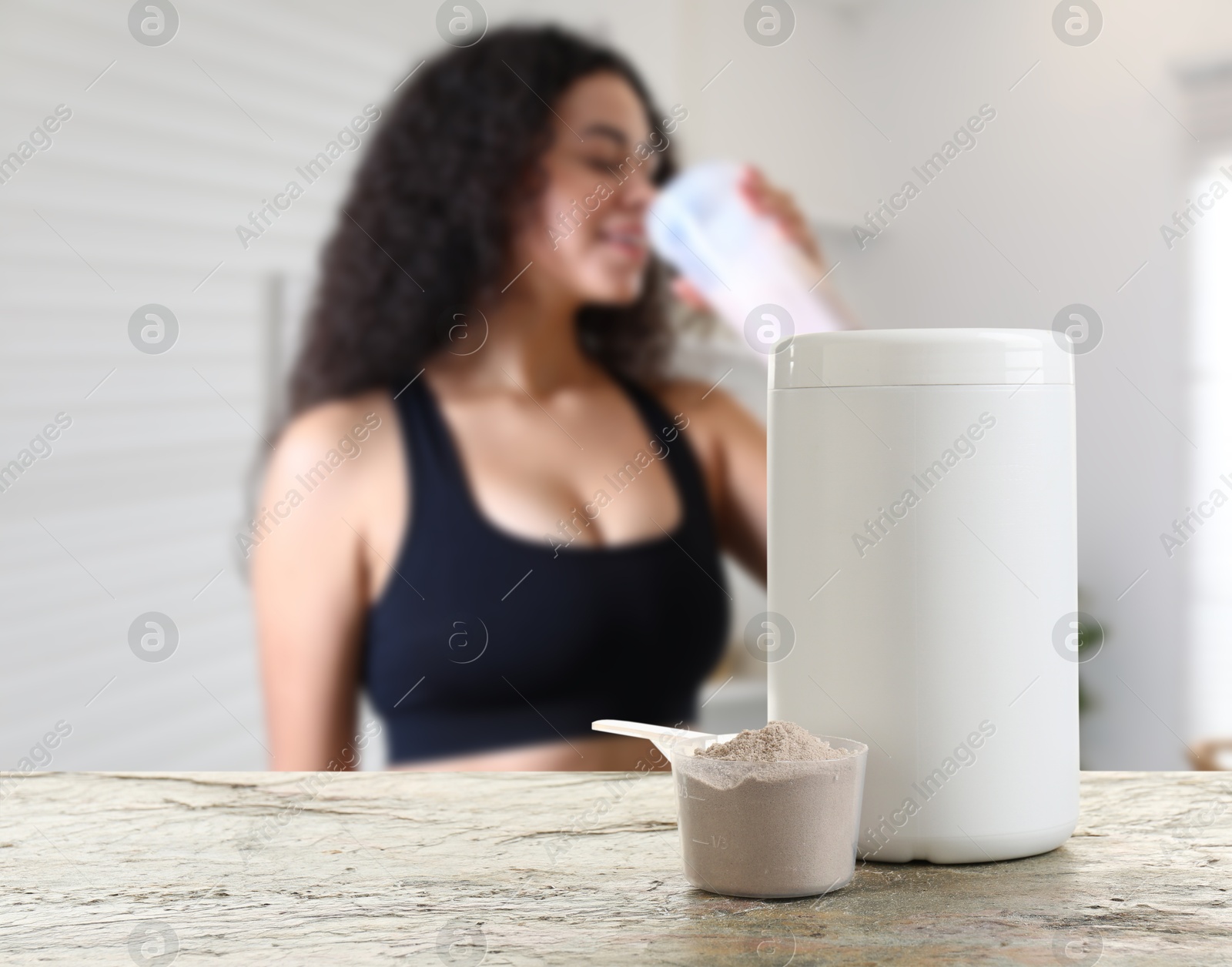 Image of Protein powder on table in room where woman drinking protein shake, selective focus